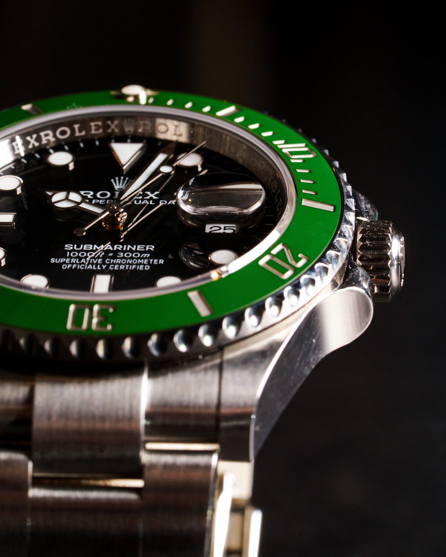 Macro shot of a Rolex Submariner watch with green bezel, showing detailed texture of dial, crown, and bracelet against a dark background