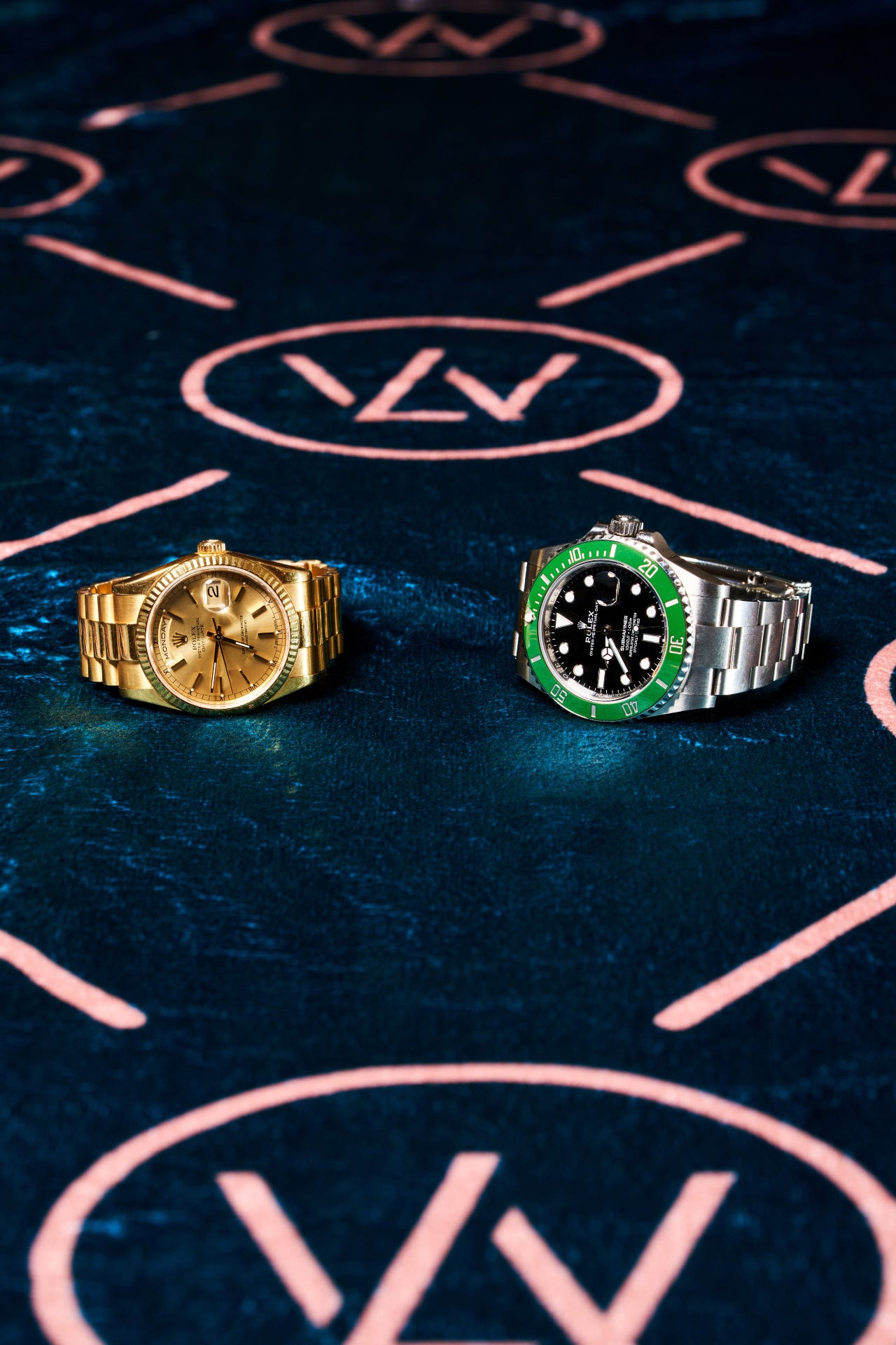 Flat lay of a gold Rolex Day-Date and a green bezel Rolex Submariner placed side by side on a Luxe Wrist branded surface